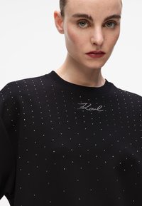 Sweatshirt preto com um padrão pontilhado de pequenos studs brilhantes e um logótipo em escrita no peito. Decote redondo e ajuste descontraído.