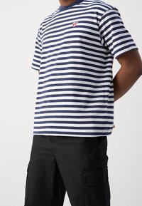 Marineblå og hvid-striped bomulds T-shirt med korte ærmer og rund halsudskæring, med et lille rødt broderet logo på brystet.