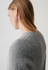 Lichtgrijze, fluffy sweater met een ronde halslijn. De textuur lijkt zacht en heeft een iets losse brei met een casual pasvorm.