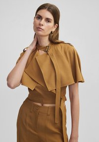 Bordeauxkleurige crop top met gedrapeerde mouwen, een gespdetail bij de nek en een soepele textuur. Gecombineerd met bijpassende high-waisted broeken.