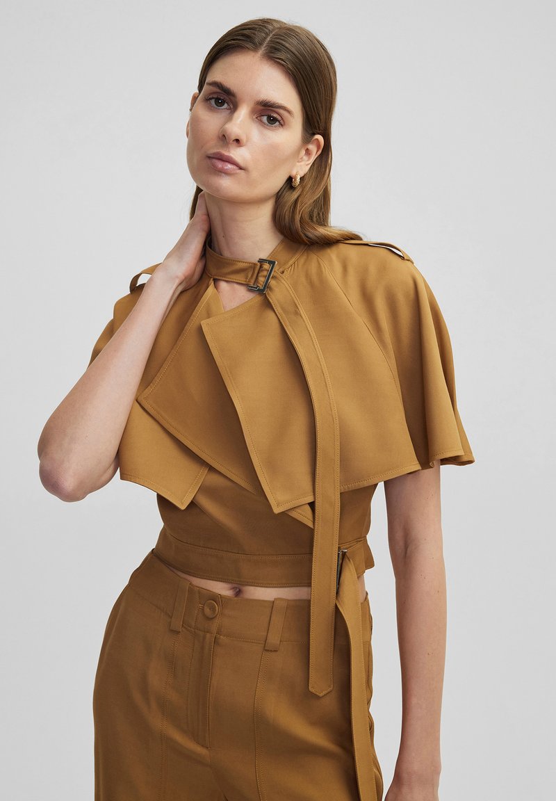 Bordeauxkleurige crop top met gedrapeerde mouwen, een gespdetail bij de nek en een soepele textuur. Gecombineerd met bijpassende high-waisted broeken.