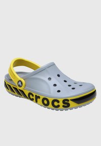 Szare plastikowe klapki z żółtym paskiem, czarnymi akcentami, otworami wentylacyjnymi oraz wyraźnym logo "crocs" z boku. Zaokrąglony czubek, lekka konstrukcja.