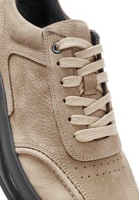 Baskets en cuir beige au toucher texturé, avec des lacets beiges, des détails perforés et une semelle en caoutchouc noire.