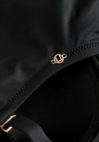 Svart simklädesmaterial med en slät textur, utrustad med guldaccessoarer och subtila sömnadsdetaljer.
