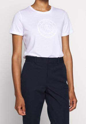 T-shirt en coton blanc avec un col rond, des manches courtes et un graphique de logo ton sur ton sur la poitrine. Associé à un pantalon sombre et ajusté.