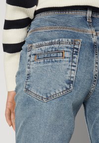 Light blue denim jeans with a back pocket featuring a rectangular patch and orange stitching, paired with a black and white striped sweater.
