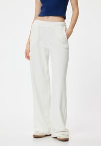 Witte, wijde broek met een elastische tailleband, voorzien van zijzakken en een zachte structuur. Gecombineerd met lichtgekleurde schoenen.