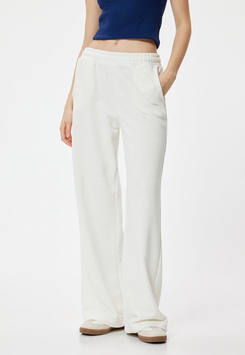 Witte, wijde broek met een elastische tailleband, voorzien van zijzakken en een zachte structuur. Gecombineerd met lichtgekleurde schoenen.