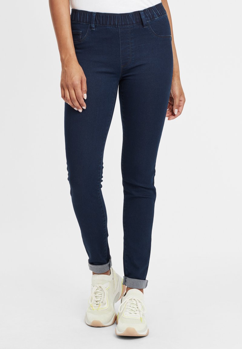 Tengerészeti kék, rugalmas farmernadrág, elasztikus derékkal, slim fit szabású és felgörgőt cuffokkal. Világos színű, párnázott sportcipővel viselve.