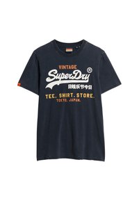 Donkerblauwe katoenen t-shirt met een ronde hals en korte mouwen. Kenmerkend zijn de witte en oranje teksten: "VINTAGE SuperDry" en "TEE. SHIRT. STORE."