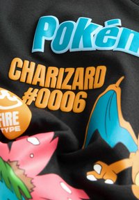 Schwarzer Stoff mit bunten Grafiken von Charizard, mit "Pokémon", "CHARIZARD #0006" und einem Feuer-Typ-Symbol in Blau und Orange.