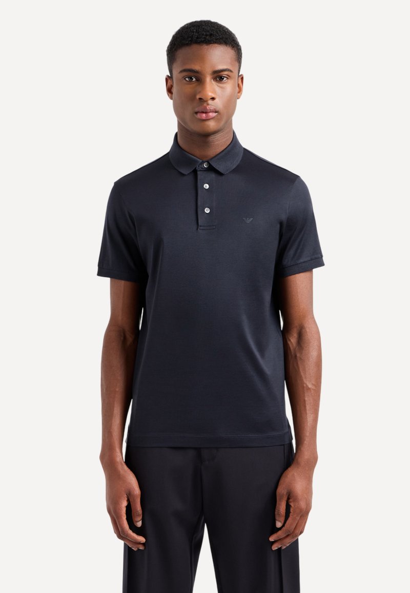 Polo shirt blu navy con una texture liscia, colletto con due bottoni, maniche corte e un logo discreto sul petto.