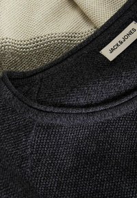Stickad tröja i en mörkgrå och beige färgpalett, med ett strukturerat mönster och en rundad halsringning med en etikett som säger "JACK & JONES."