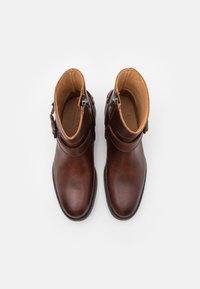 Botas de tobillo de cuero marrón con una textura suave, que cuentan con una cremallera lateral y un detalle de correa ajustable alrededor del tobillo.
