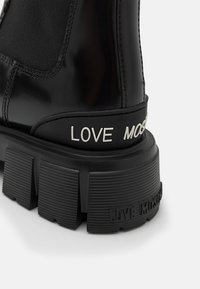 Bottines noires brillantes avec des panneaux élastiques, semelle en caoutchouc épaisse et texte embossé "LOVE MOSCHINO" sur le côté et à l'arrière. Talon texturé.