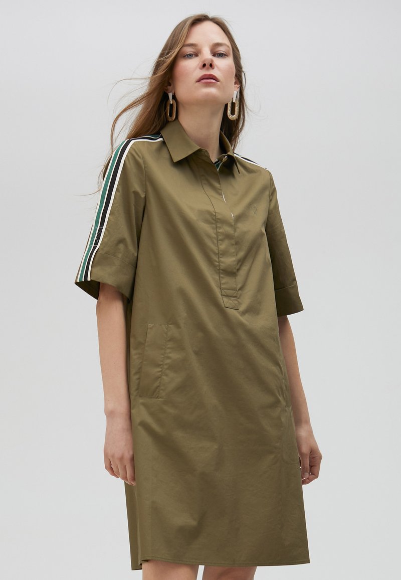 Olive green dress with a collared neck, short sleeves, and two side pockets. Features contrasting stripes on sleeves and a button-less placket.