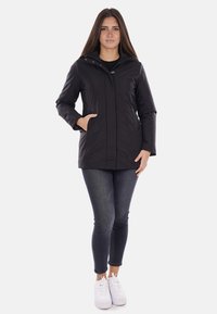 Giacca nera impermeabile con chiusura a zip e bottoni automatici, due tasche laterali e cappuccio. Presenta una texture liscia e un design elegante.