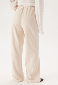 Crème-kleurige wijde broek met een gladde, vloeiende textuur en een elastische tailleband, gecombineerd met een zachte, lichte trui.