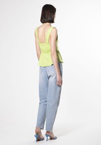 Top peplo in lino verde lime con spalline larghe e schiena scoperta, abbinato a jeans in stile vintage azzurri e scarpe con tacco blu.