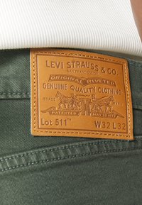 Patch en cuir Levi Strauss & Co. sur un jean en denim vert indiquant le nom de la marque, "Original Riveted," "Lot 511," et la taille W32 L32.