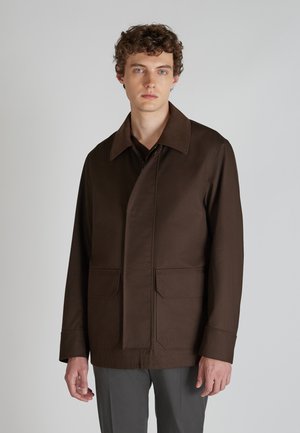 Brauner, mittellanger Mantel mit Spread-Kragen, geradem Schnitt, frontalen Taschen und auffälligen Nähten. Hergestellt aus glattem Stoff, minimalistisches Design.
