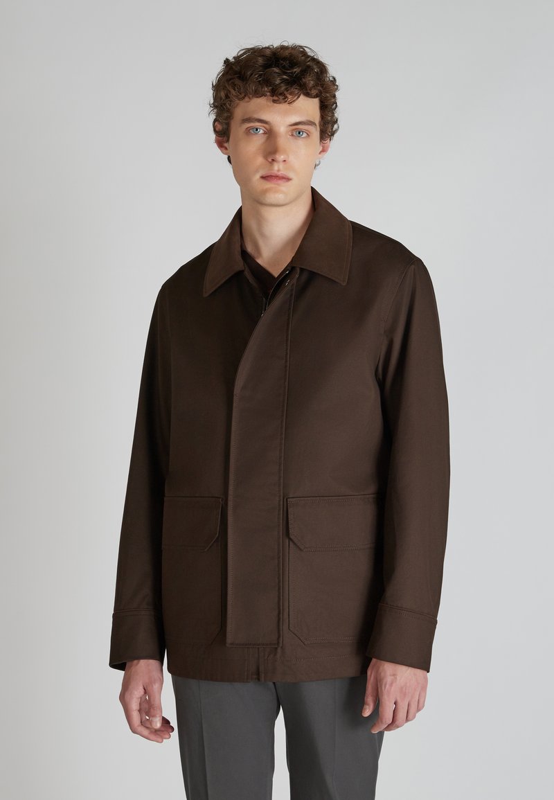 Abrigo marrón de longitud media con cuello extendido, corte recto, bolsillos delanteros y costuras visibles. Confeccionado en tejido suave, diseño minimalista.