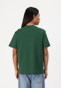 T-shirt verde in cotone con maniche corte e scollo rotondo. Colore uniforme senza fantasie, indossato con jeans in denim azzurro chiaro.