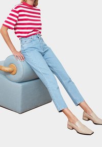 Osoba oblečená v červeno-bílém pruhovaném tričku, světle modrých kalhotách s vysokým pasem a béžových nízkých podpatcích, sedící na světle modrém čalouněném stoličce.