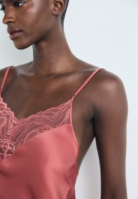 Rosa satengcamisole med delikat blonder trim rundt halsen, tynne justerbare stropper og en jevn tekstur.