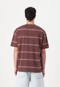 Brown short-sleeve t-shirt with pink horizontal stripes, round neckline, and relaxed fit, shown from the back on a model.