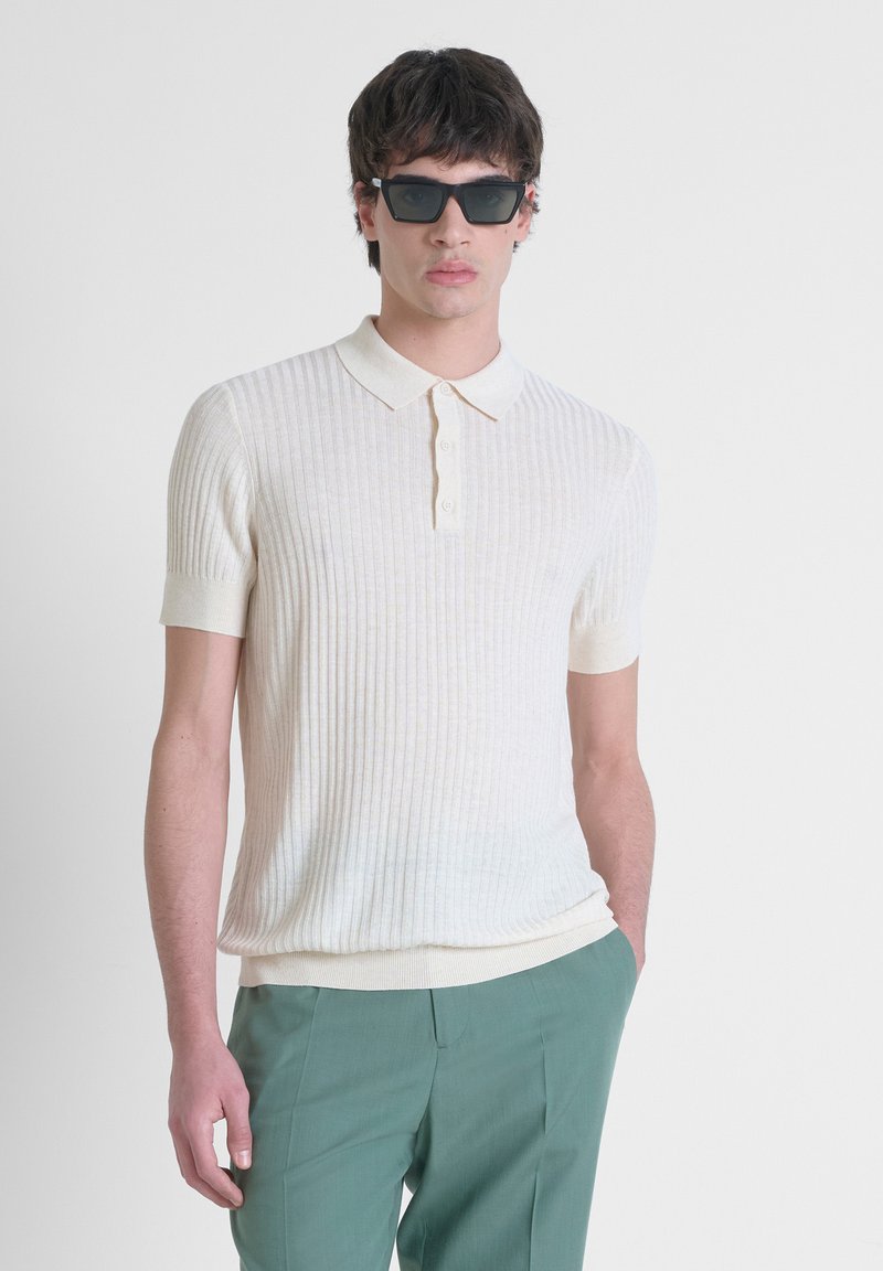 Polo shirt a costine crema con maniche corte, dotato di colletto piatto e placket con tre bottoni, abbinato a pantaloni verdi su misura.