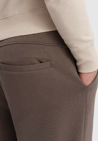 Brune sweatpants med en blød tekstur, som har en baglomme og en beige sweatshirt. Designet fremhæver komfort og afslappet påklædning.