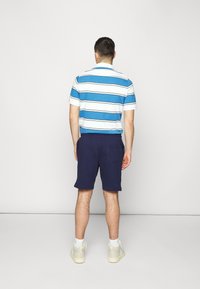 Paski niebiesko-biały polo z krótkim rękawem, w połączeniu z granatowymi szortami. Białe skarpetki i jasne sneakersy dopełniają zestaw.