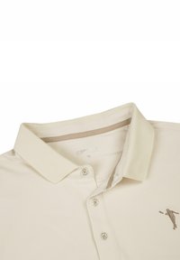 Beige poloshirt met kraag, drie knopen en een geborduurd logo. Het materiaal lijkt een structuur te hebben met een subtiel patroon. Maat: M.
