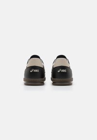 Baskets de sport noires et beiges en cuir texturé, avec des accents cousus et un détail de logo sur le talon ; design bas pour un enfilage facile.