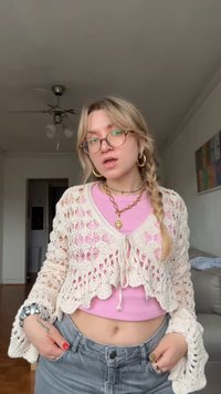 Cardigan croșetat în crema cu model cu perforații, purtat peste un top roz strâmt din material răzuit, asociat cu pantaloni scurți gri cu talie înaltă. Accesorii argintii.