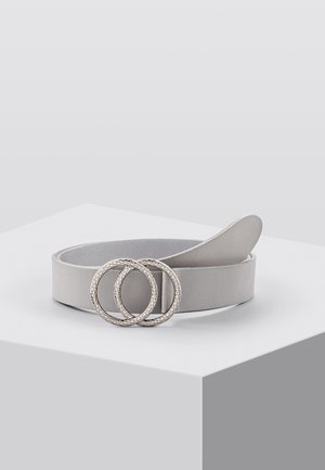 Jasnoszary pasek z teksturowaną metalową sprzączką w kształcie podwójnego pierścienia, zwinięty i wyeksponowany na białym podeście na tle jasnoszarym.