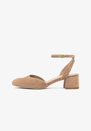 Beżowy zamszowy but na niskim obcasie typu słupek, z zamkniętym, zaokrąglonym noskiem, odkrytymi bokami oraz regulowanym paskiem wokół kostki z złotą klamrą.