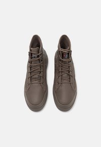 Pár hnědých kožených vysokých tenisek s tkaničkami a štítky s izolací 3M Thinsulate, zobrazených z vrchu na bílém pozadí.