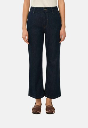 Jeans blu scuro a gamba larga indossati con scarpe mocassino con frange marroni e una maglia bianca, mostrati dalla vita ai piedi.