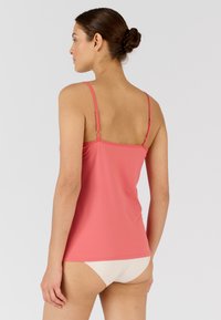 Top in corallo con spalline sottili, morbido al tatto, design aderente e schiena dritta. Abbinarlo a una mutanda da bagno di colore neutro.