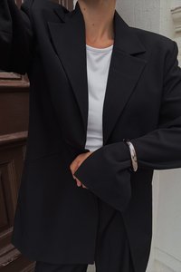 Prevelik črn blejzer iz teksturirane tkanine, z nazubljenimi klapnicami in širokimi zapestji. Kombiniran z belim zgornjim delom in srebrnim uhani.