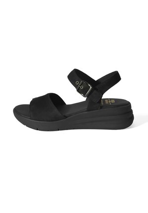 Zwarte sandaal met open teen, verstelbare enkelriem, gespsluiting, gevoerde zool en een kleine sleehak tegen een witte achtergrond.