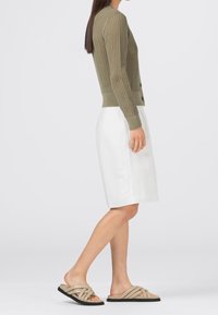 Olivgrön stickad cardigan med strukturerad mönster, knäppning; parat med en vit knälång kjol och beige krossbandssandaler.