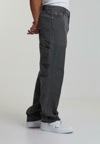 Grå cargo bukser med teksturert finish, flere lommer og brodert merkevaredetalj, kombinert med hvite sneakers.