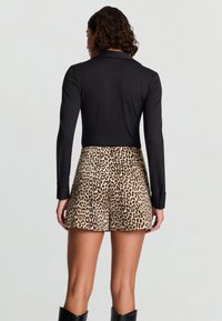 Top nero a maniche lunghe abbinato a pantaloncini con stampa leopardata, caratterizzati da un design aderente e una texture liscia. Sono visibili stivali neri con suola di gomma.