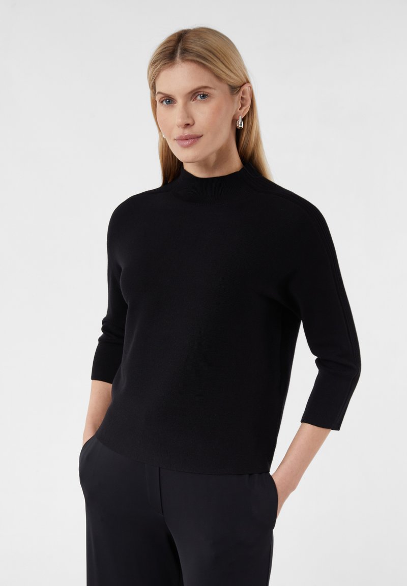 Schwarzer Strickpullover mit hohem Kragen und Dreiviertelärmeln, glatte Textur, mit dezenten Schulterdetails und einer lockeren Passform.