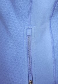 Himmelblaues Fleece-Material mit einem vertikalen Reißverschluss in der Mitte, das eine glatte Textur und verstärkte Nähte entlang der Kanten aufweist.