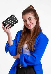 Černá peněženka s bílými puntíky, kožený materiál, na zip. Modelka ji předvádí v modrém saku a černých kalhotách.