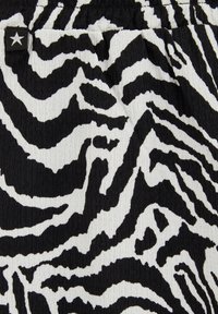 Tkanina z vzorcem zebra v črno-beli barvi, ki ima teksturirano površino. Značilne valovite črte ustvarjajo vizualni kontrast in globino.